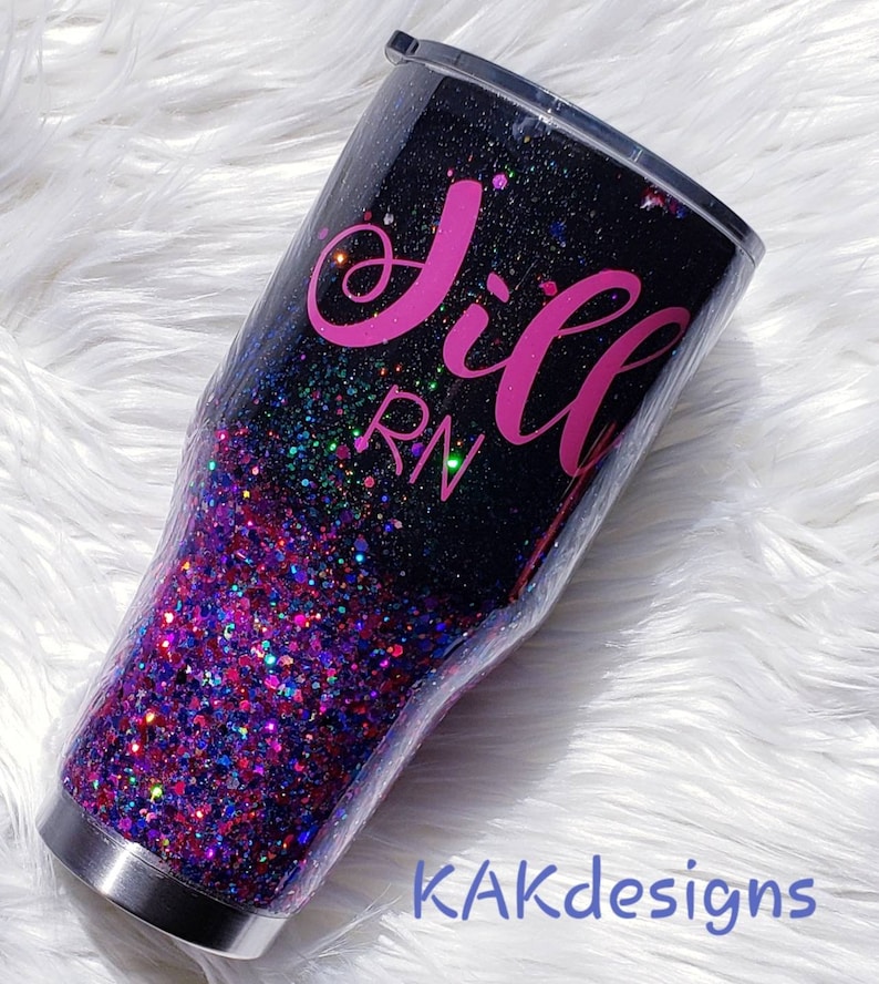 May include: A black and pink glitter tumbler with the name "Jill RN" written on it.