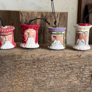 May include: Four hand-painted wooden spool ornaments featuring bearded figures with distinct hats. Each spool has a black string loop at the top. The figures are painted in red, white, green, and purple with detailed facial features and white beards.