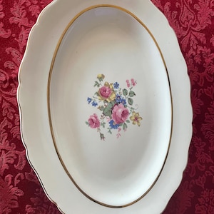 Puede incluir: Plato ovalado blanco para servir con un borde dorado y un diseño floral en el centro. Las flores son rosas, amarillas y azules.