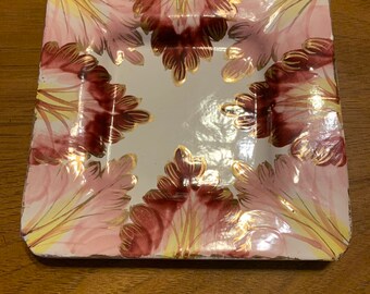 May include: Square ceramic plate with a pink, white, and gold floral design. The plate has a raised edge and a glossy finish.