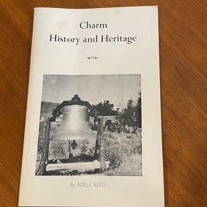 May include: A black and white photo of a bell hanging from a wooden frame. The bell is in front of a building with a grassy area in the foreground. The text "Charm History and Heritage" is at the top of the page and the text "By ADELE REED" is at the bottom of the page.