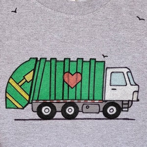 May include: A gray t-shirt with a green and white garbage truck graphic. The truck has a red heart on the side and a yellow and green recycling bin in the back.