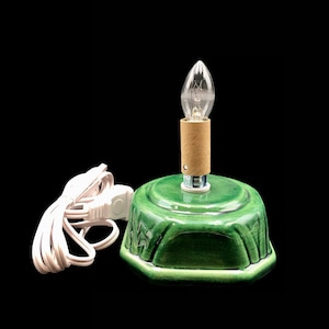 May include: A green ceramic base with a light bulb and cord. The base has a decorative design and is used for a Christmas tree.