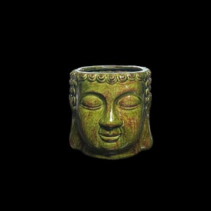 May include: A green ceramic Buddha head planter with closed eyes and a serene expression. The planter has a wide opening and is suitable for small plants or succulents. The Buddha head is a decorative item.