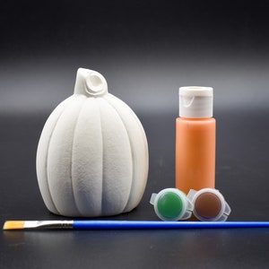 May include: White ceramic pumpkin with a stem, a bottle of orange paint, two small pots of green and brown paint, and a blue paintbrush.