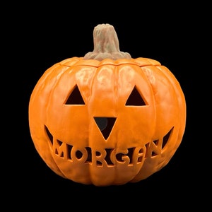 May include: Orange ceramic pumpkin with a carved jack-o'-lantern face and the name "MORGAN" carved into the bottom.