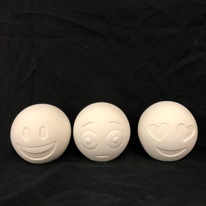 May include: Three white ceramic emoji ornaments with different facial expressions: a smiling face, a surprised face, and a face with hearts for eyes.