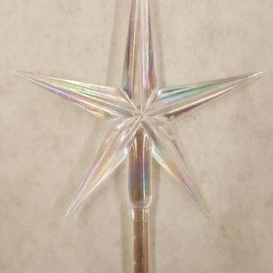 May include: A clear iridescent plastic star tree topper with a pointed tip and a long, thin stem.