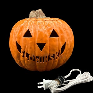 May include: An orange plastic jack-o'-lantern with a carved face and the name "Slowinski" on the front. The jack-o'-lantern has a light bulb inside and a white cord with a plug.