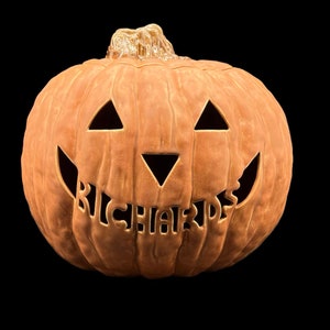 May include: A brown ceramic pumpkin with a carved jack-o'-lantern face and the word "RICHARDS" carved into the bottom of the face.