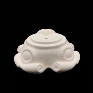 May include: White ceramic base with a round top and a decorative design of scrolls and circles around the bottom.