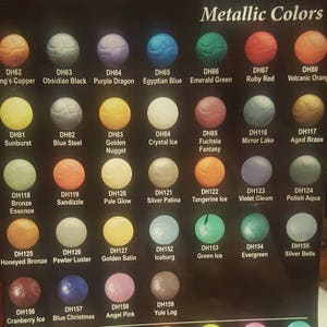 May include: A chart of metallic paint colors with names and corresponding color swatches. The colors include King's Copper, Obsidian Black, Purple Dragon, Egyptian Blue, Emerald Green, Ruby Red, Volcanic Orange, Sunburst, Blue Steel, Golden Nugget, Crystal Ice, Fuchsia Fantasy, Mirror Lake, Aged Brass, Bronze Essence, Sandizzle, Pale Glow, Silver Patina, Tangerine Ice, Violet Gleam, Polish Aqua, Honeyed Bronze, Pewter Luster, Golden Satin, Iceburg, Green Ice, Evergreen, Silver Bells, Cranberry Ice, Blue Christmas, Angel Pink, and Yule Log.