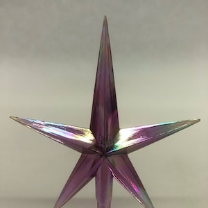 Peut inclure: Une étoile de Noël à cinq branches de couleur violette irisée. L'étoile a un sommet pointu et une longue tige fine.