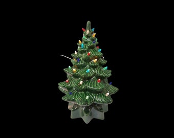 May include: A green ceramic Christmas tree with colorful lights. The tree has a star-shaped base and is decorated with red, yellow, blue, and green lights.
