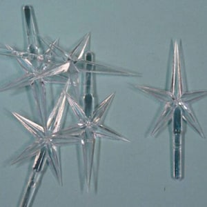 May include: A set of six clear plastic star-shaped Christmas tree toppers. The stars have six points and are attached to a clear plastic stem.