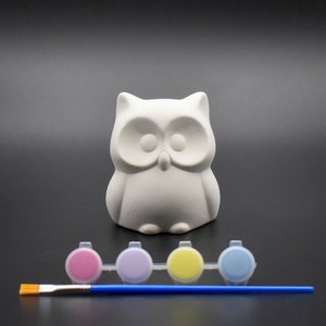 May include: White ceramic owl figurine with paint pots and a paintbrush. The paint pots are pink, purple, yellow, and blue.