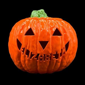 May include: Orange ceramic pumpkin with a carved jack-o'-lantern face and the name "Elizabeth" carved into the bottom.