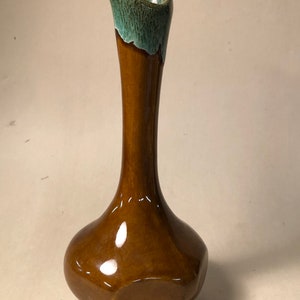 May include: A brown ceramic vase with a flared opening and a green glaze on the top. The vase has a rounded body with a slightly pointed base.