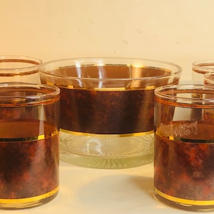 May include: Set of six brown and gold glasses with a matching ice bucket. The glasses have a brown and gold marbled design with a gold band around the top.