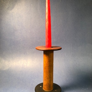 May include: A wooden candle holder with a black base and a red candle. The candle holder is made from a wooden spool.