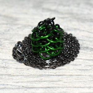May include: A green and black chainmail pendant necklace. The pendant is a sphere shape and is made of metal rings. The necklace is a black chain.