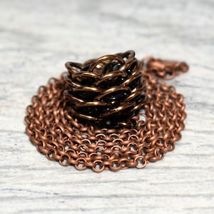 May include: A copper chain necklace with a black and copper chainmail ring pendant.
