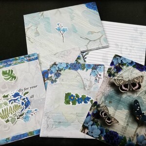May include: A set of blue and white stationery featuring floral and butterfly designs. The set includes envelopes, note cards, and lined paper. The text "The lan Studio Stationery Shoppe" is visible on one of the envelopes.