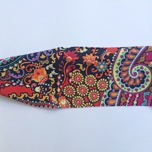 May include: A colorful paisley patterned headband in shades of red, orange, yellow, green, blue, and purple on a black background.
