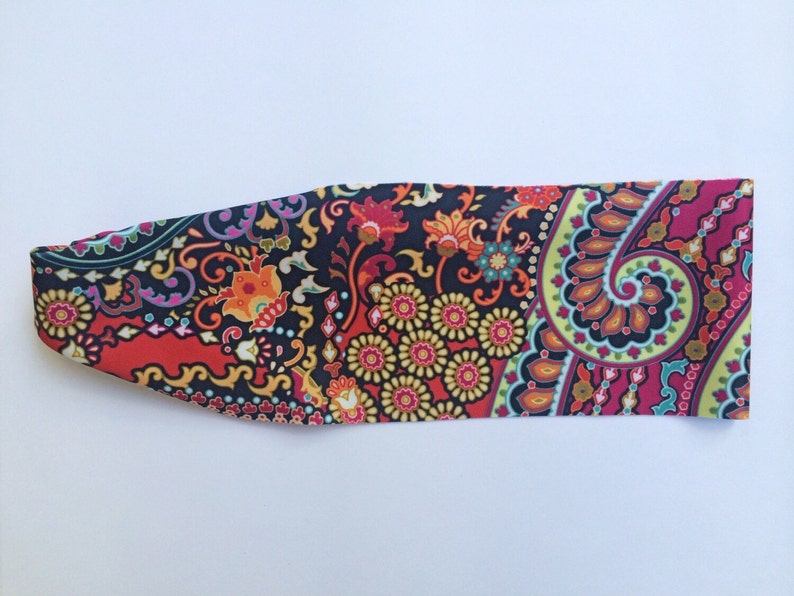 May include: A colorful paisley patterned headband in shades of red, orange, yellow, green, blue, and purple on a black background.