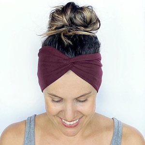 May include: A burgundy knotted headband made of soft fabric. The headband is worn by a person with brown hair pulled back in a bun.