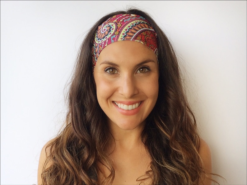 May include: A woman with long brown hair is wearing a patterned headband with red, green, yellow, and blue colors. The headband is made of a soft, stretchy fabric.