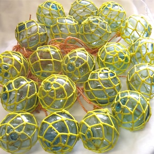 May include: A group of glass fishing floats with yellow netting. The floats are various shades of blue and green.