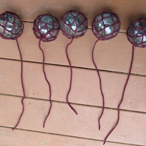 May include: Six glass floats with burgundy netting and strings hanging from a wooden surface.