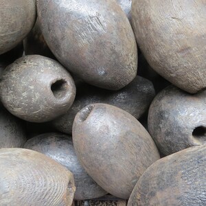 May include: A collection of weathered, dark gray wooden buoys. The buoys are oval-shaped with a hole drilled through the center. The wood grain is visible on the surface of the buoys. The buoys are likely used for nautical purposes.