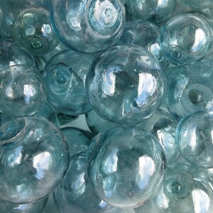 May include: A close-up of a group of blue glass fishing floats. The floats are round and have a smooth, shiny surface. They are arranged in a random pattern, with some overlapping.