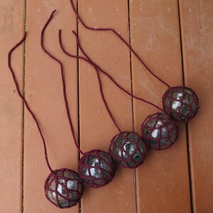 May include: Six glass floats with burgundy netting, hanging from burgundy cords. The floats are round and have a white, cloudy appearance.