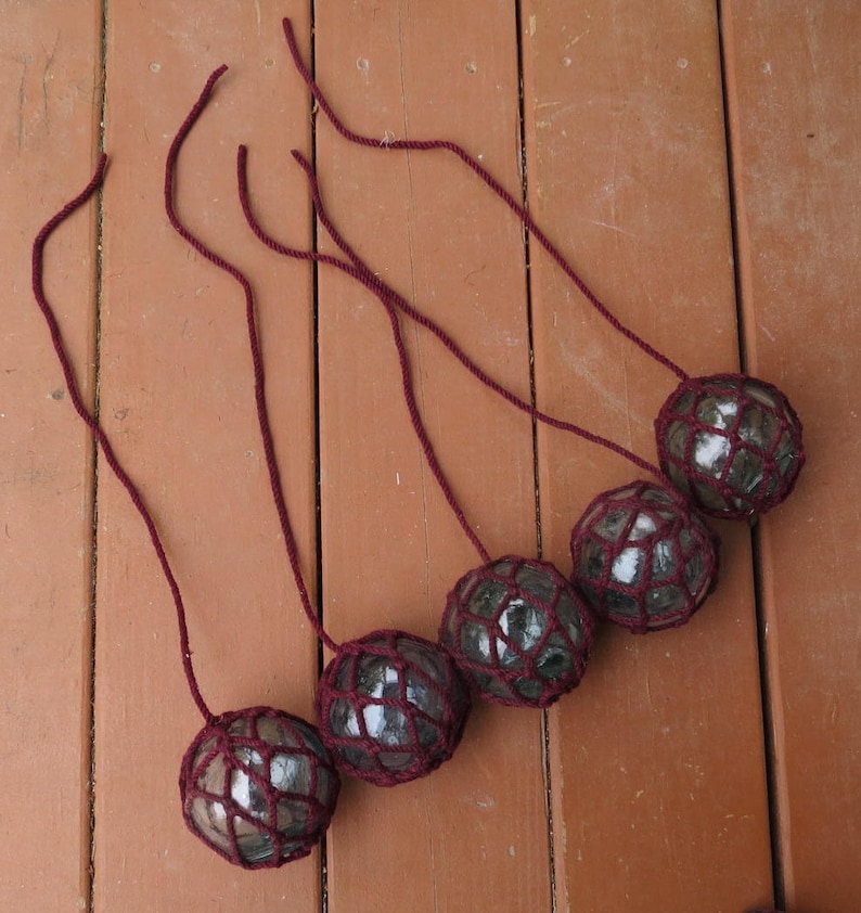 May include: Six glass floats with burgundy netting, hanging from burgundy cords. The floats are round and have a white, cloudy appearance.