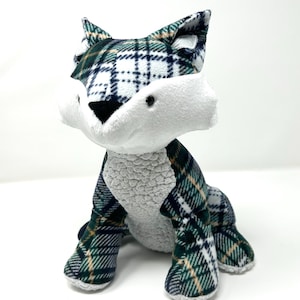 May include: A plush fox toy with a white muzzle and belly, and a green, navy, and tan plaid pattern on its ears, legs, and back. The fox has a gray textured body and is sitting upright.