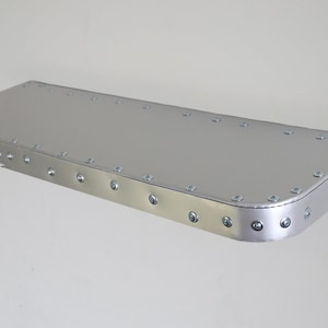 Op de afbeelding: Een zilveren metalen plank met een afgeronde rand en een rij klinknagels rondom de omtrek.