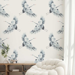 May include: A white room with a white couch and two white ottomans. The wall is covered in a wallpaper with a pattern of blue cranes.