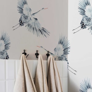 May include: Three beige towels hanging on hooks against a wall with a watercolor pattern of blue cranes.