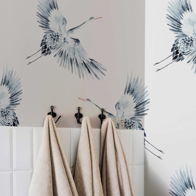 May include: Three beige towels hanging on hooks against a wall with a watercolor pattern of blue cranes.