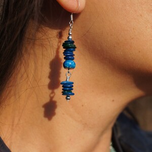 May include: A pair of dangle earrings featuring blue and green wooden beads. The earrings are made of metal.