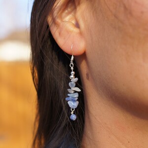 May include: A pair of silver dangle earrings with blue gemstone chips. The earrings are long and feature a variety of blue shades.