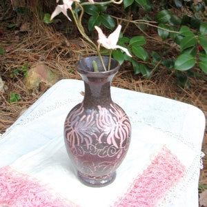 May include: A dark brown ceramic vase with a pink floral design. The vase is filled with dried white flowers.