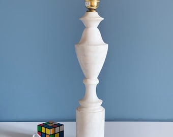 Peut inclure: Une lampe de table en albâtre blanc avec une douille dorée et un cordon blanc. La lampe est posée sur une surface blanche avec un Rubik's Cube coloré au premier plan.
