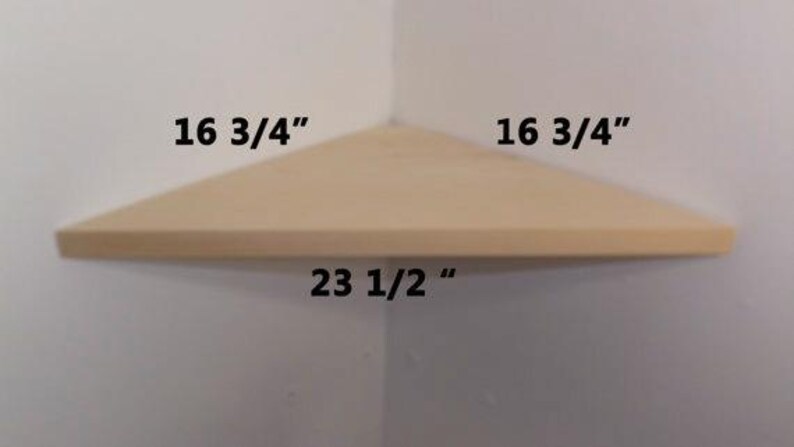 May include: A light-colored wooden corner shelf with a triangular shape. The dimensions are printed on the image as 16 3/4 inches for the two sides that meet the wall and 23 1/2 inches for the front edge facing outward from the corner.