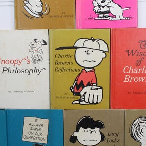 May include: A collection of ten vintage Peanuts paperback books featuring Charlie Brown and Snoopy. The books are in various colors, including red, blue, yellow, and green. The titles include "Snoopy's Philosophy", "Charlie Brown's Reflections", "The Wisdom of Charlie Brown", "Everything I Do Makes Me Feel Guilty", "It Always Rains on Our Generation", and "Lucy Looks".