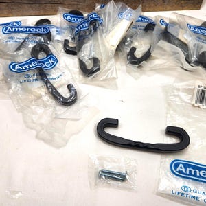 May include: A collection of black Amerock hooks, some still in their original packaging. The hooks are in various sizes and shapes, with a curved design. The image also shows screws and a larger handle.