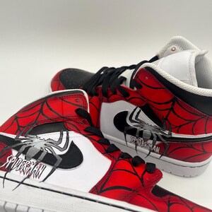Puede incluir: Par de zapatillas altas con tem&aacute;tica de Spider-Man. Los zapatos presentan una combinaci&oacute;n de colores rojo y negro con un dise&ntilde;o de telara&ntilde;a y la palabra "SPIDERMAN" impresa en el lateral. Las suelas son blancas.